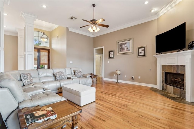 living room with light hardwood / wood-style flooring, ceiling fan, decorative columns, ornamental molding, and a tiled fireplace