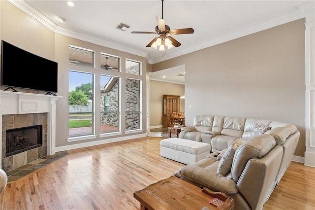 living room with a tiled fireplace, ceiling fan, ornamental molding, and light wood-type flooring