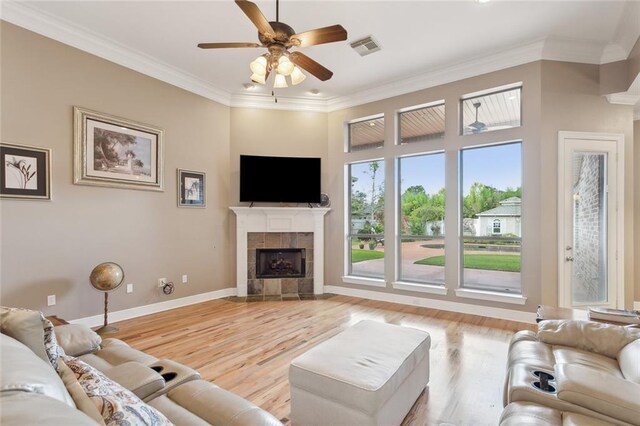 living room featuring visible vents, light wood finished floors, a fireplace, ornamental molding, and a ceiling fan