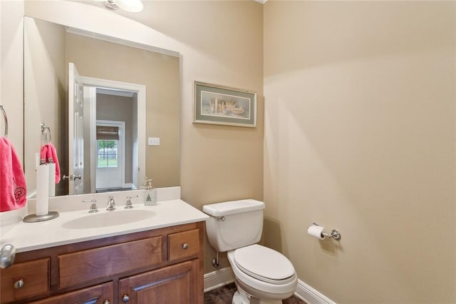 half bathroom featuring toilet, vanity, and baseboards