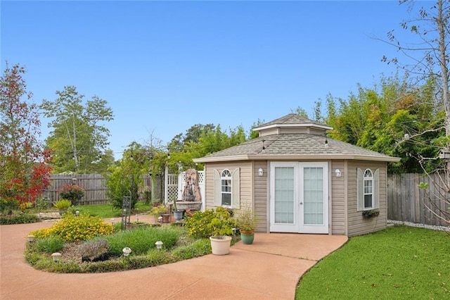 back of house with an outdoor structure, fence, french doors, a shingled roof, and a yard