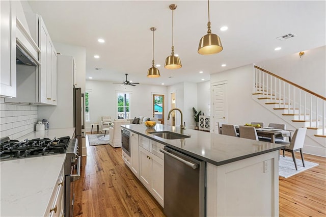 kitchen featuring sink, white cabinetry, hanging light fixtures, stainless steel appliances, and a kitchen island with sink