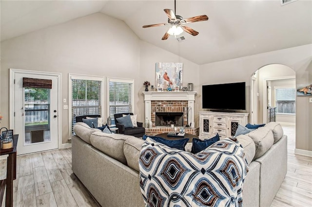 living room with ceiling fan, a brick fireplace, high vaulted ceiling, and light hardwood / wood-style flooring