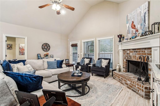 living room featuring ceiling fan, a fireplace, high vaulted ceiling, and light wood-type flooring