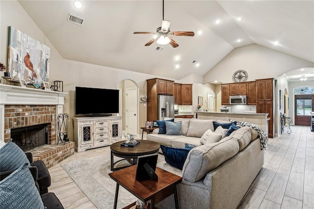 living room with a brick fireplace, light hardwood / wood-style flooring, high vaulted ceiling, and ceiling fan