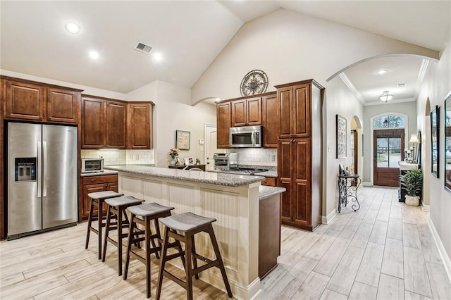 kitchen with a kitchen bar, a center island, stainless steel appliances, light stone countertops, and light wood-type flooring