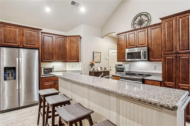 kitchen with stainless steel appliances, a kitchen breakfast bar, light stone countertops, and backsplash