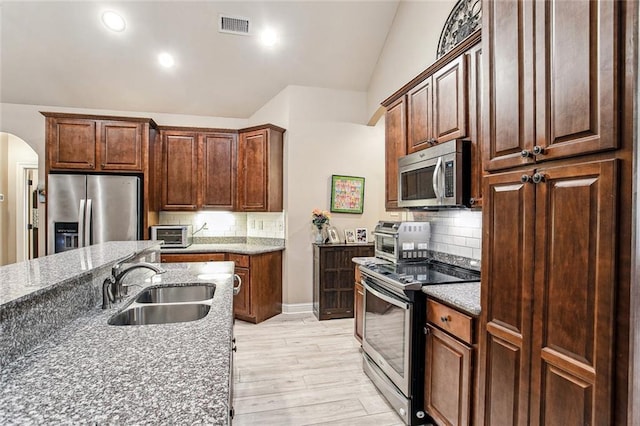 kitchen with sink, vaulted ceiling, light hardwood / wood-style flooring, appliances with stainless steel finishes, and dark stone counters