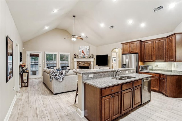 kitchen with sink, light hardwood / wood-style flooring, appliances with stainless steel finishes, an island with sink, and a fireplace