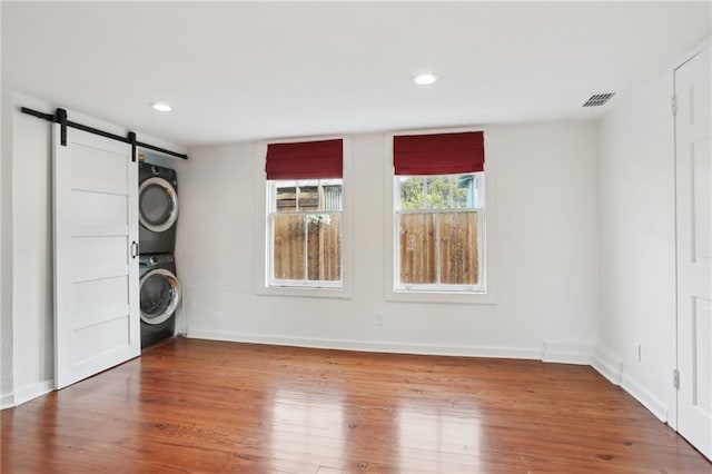 laundry room with stacked washer / dryer, a barn door, and hardwood / wood-style flooring