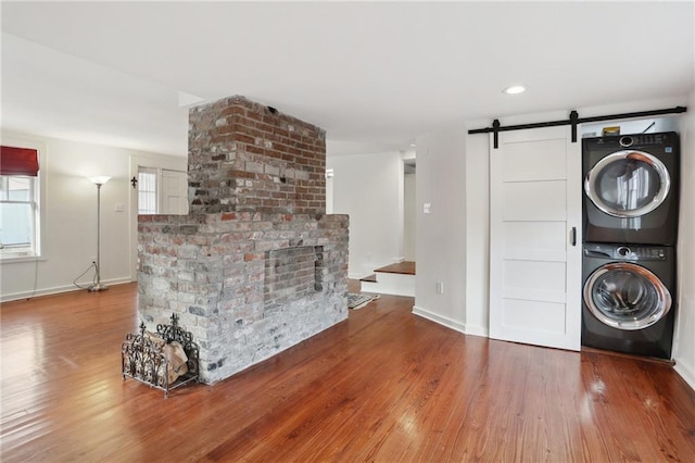 laundry area featuring hardwood / wood-style flooring, a fireplace, stacked washer and clothes dryer, and a barn door