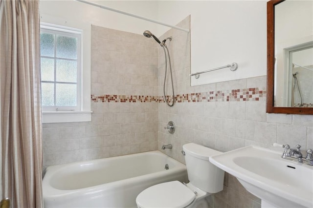 full bathroom featuring tiled shower / bath, toilet, sink, and tile walls