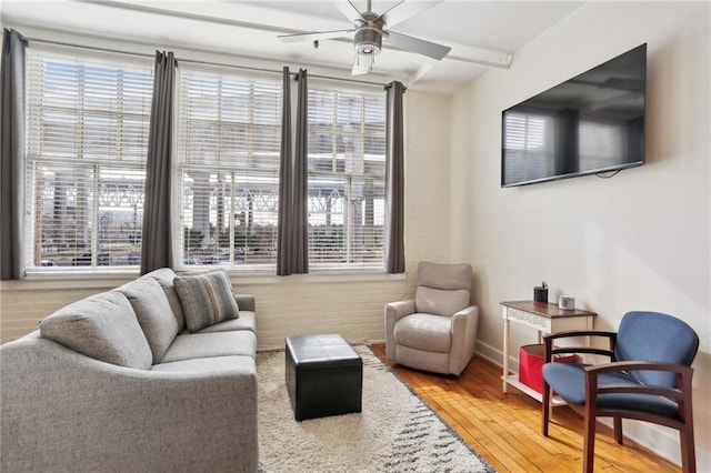 living area featuring beamed ceiling, ceiling fan, and wood-type flooring