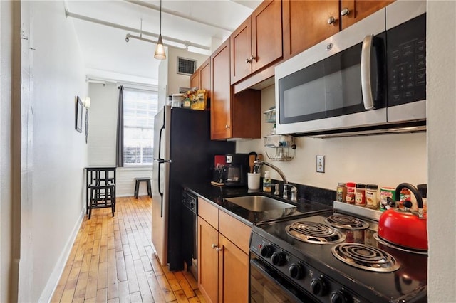 kitchen with sink, decorative light fixtures, light hardwood / wood-style flooring, dark stone countertops, and black appliances