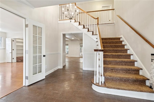 stairway with an inviting chandelier, a high ceiling, wood-type flooring, ornamental molding, and french doors