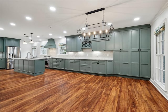 kitchen featuring sink, custom exhaust hood, hanging light fixtures, appliances with stainless steel finishes, and a kitchen island with sink