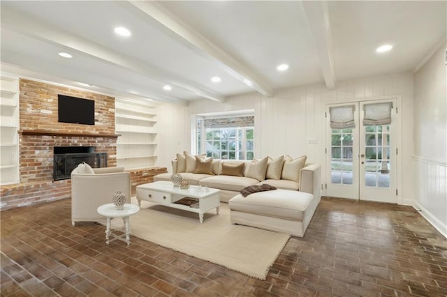 living room with a brick fireplace, beam ceiling, and built in shelves