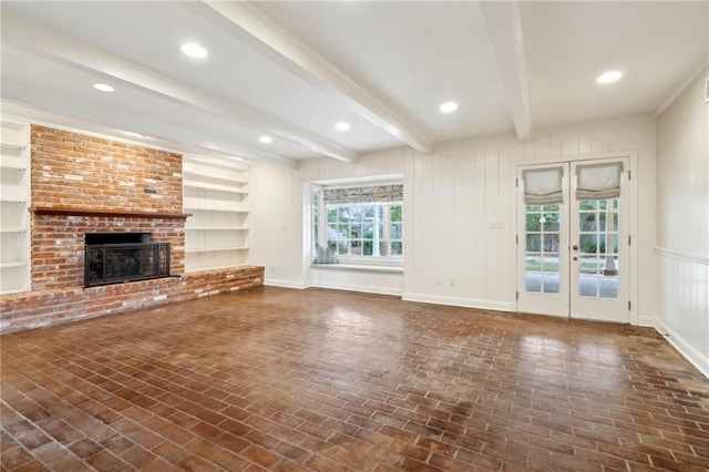 unfurnished living room featuring a brick fireplace, built in features, beam ceiling, and french doors