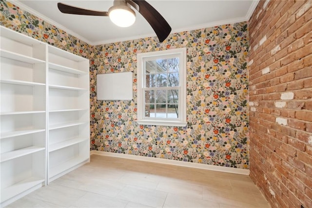 empty room with crown molding, ceiling fan, and brick wall