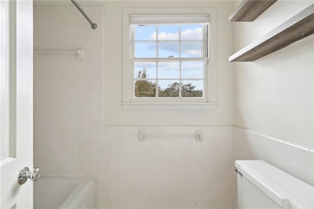 bathroom featuring washtub / shower combination, toilet, and tile walls