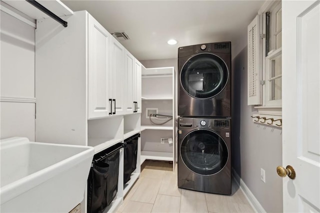 laundry room featuring light tile patterned flooring, cabinets, stacked washer / dryer, and sink