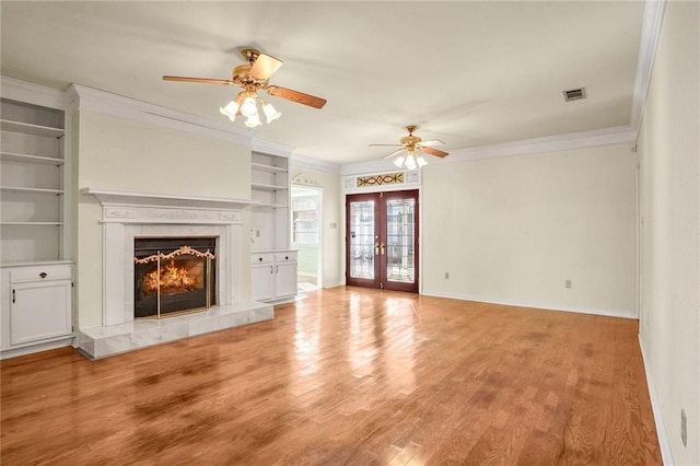 unfurnished living room featuring a tile fireplace, ornamental molding, light hardwood / wood-style flooring, and french doors