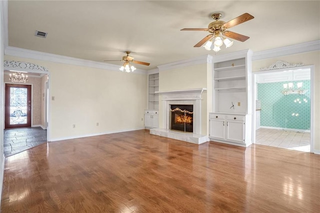 unfurnished living room featuring ornamental molding, wood-type flooring, ceiling fan with notable chandelier, and built in features