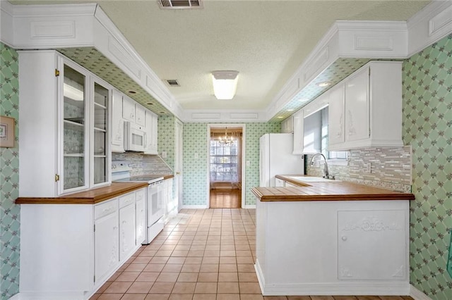 kitchen with sink, white appliances, light tile patterned floors, white cabinetry, and kitchen peninsula