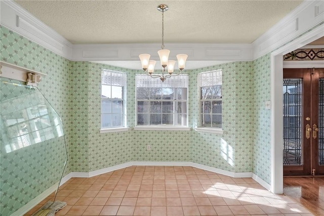 unfurnished dining area with light tile patterned floors, crown molding, a textured ceiling, french doors, and a chandelier