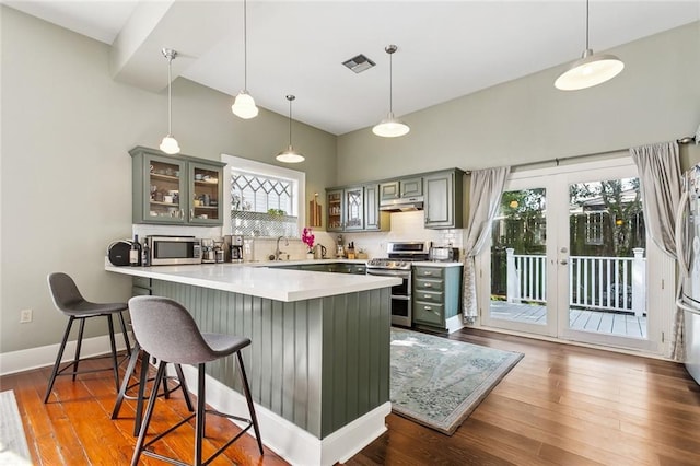 kitchen featuring a kitchen breakfast bar, stainless steel appliances, backsplash, under cabinet range hood, and glass insert cabinets