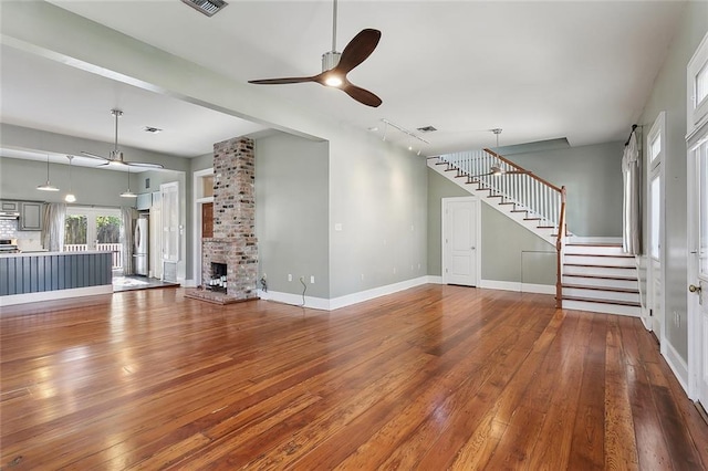unfurnished living room with a ceiling fan, visible vents, stairway, baseboards, and hardwood / wood-style floors