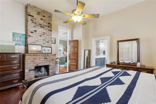 bedroom featuring a fireplace, a ceiling fan, ensuite bath, and wood finished floors