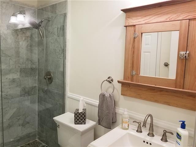 bathroom with tiled shower, toilet, and sink