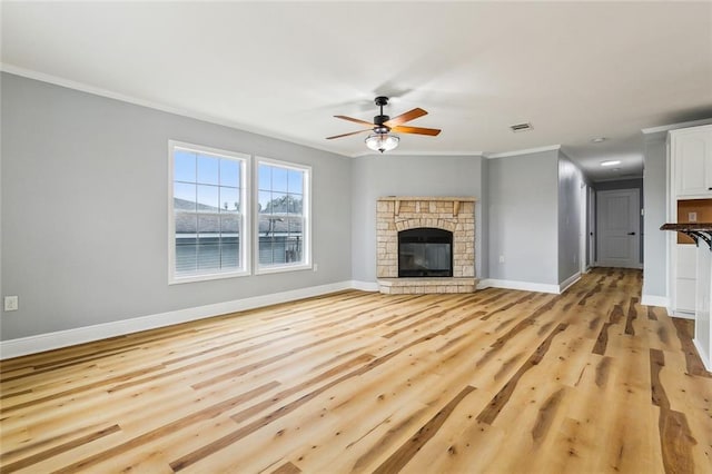 unfurnished living room with ornamental molding, a stone fireplace, ceiling fan, and light wood-type flooring