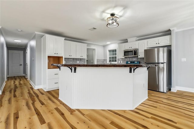 kitchen with appliances with stainless steel finishes, light hardwood / wood-style floors, a breakfast bar area, and white cabinets