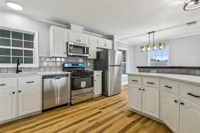 kitchen featuring sink, white cabinetry, pendant lighting, stainless steel appliances, and decorative backsplash