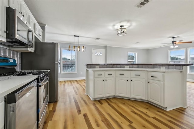 kitchen with white cabinetry, hanging light fixtures, backsplash, stainless steel appliances, and light hardwood / wood-style floors