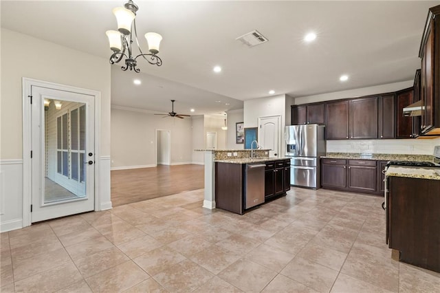 kitchen featuring extractor fan, hanging light fixtures, stainless steel appliances, light stone countertops, and a center island with sink