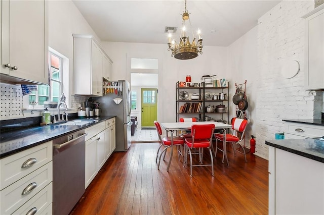 kitchen featuring sink, dark wood-type flooring, appliances with stainless steel finishes, white cabinetry, and decorative light fixtures