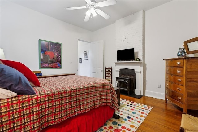 bedroom featuring hardwood / wood-style flooring, ceiling fan, and a wood stove