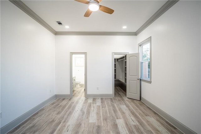 unfurnished bedroom featuring crown molding, a walk in closet, light wood-type flooring, and a closet