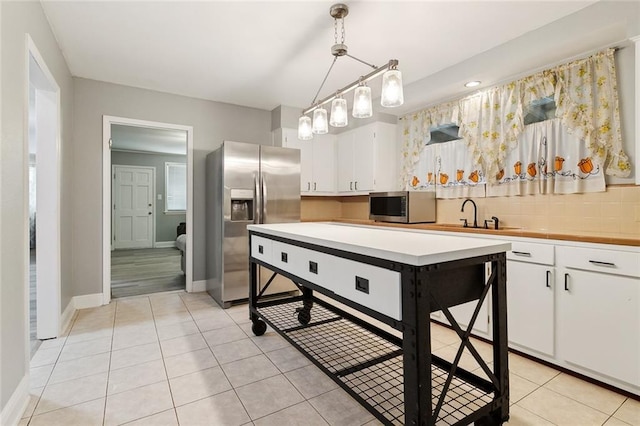 kitchen featuring light tile patterned floors, appliances with stainless steel finishes, hanging light fixtures, tasteful backsplash, and white cabinets