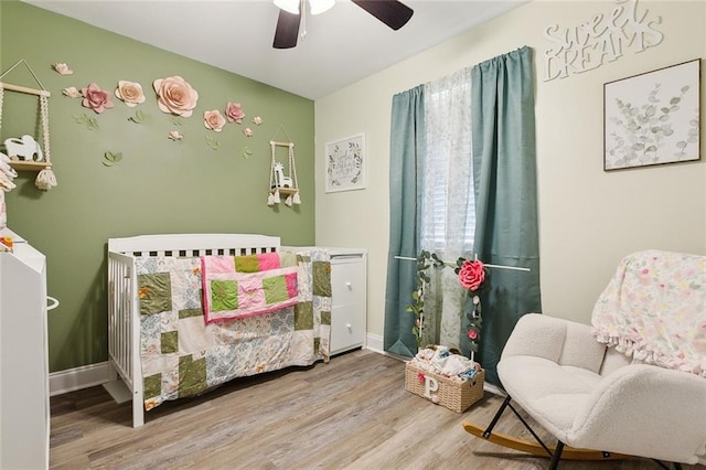 bedroom with hardwood / wood-style floors, a crib, and ceiling fan