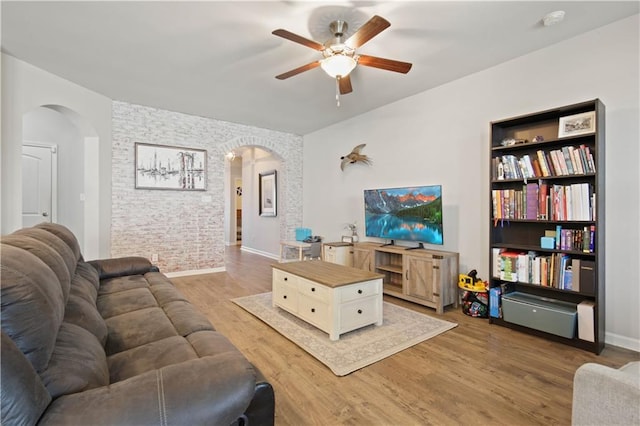 living room featuring hardwood / wood-style flooring, brick wall, and ceiling fan