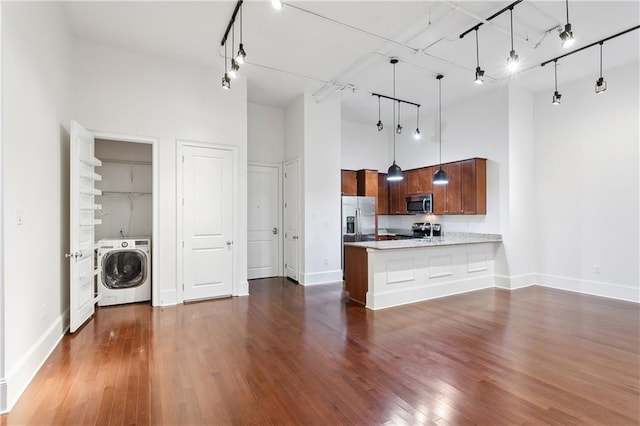 kitchen featuring dark wood-type flooring, washer / dryer, appliances with stainless steel finishes, kitchen peninsula, and a high ceiling