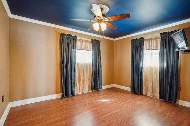 spare room featuring baseboards, wood finished floors, a ceiling fan, and crown molding