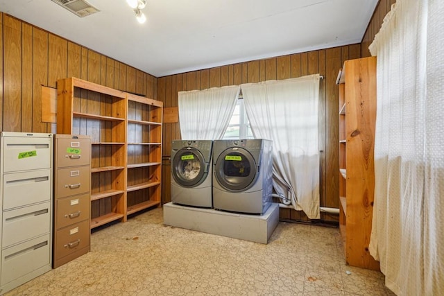 washroom featuring washer and dryer, visible vents, wooden walls, and light floors