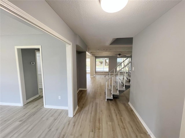 corridor with light wood-type flooring and a textured ceiling