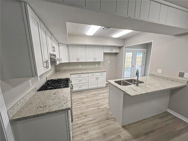 kitchen featuring sink, light stone counters, light wood-type flooring, kitchen peninsula, and white cabinets