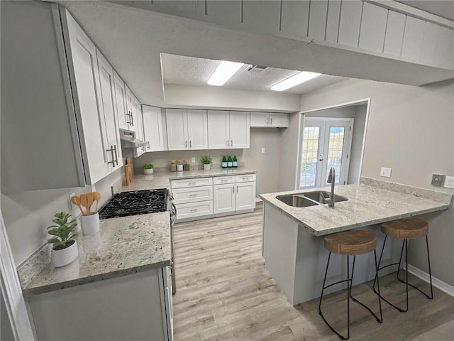 kitchen featuring sink, light hardwood / wood-style floors, kitchen peninsula, white cabinets, and french doors